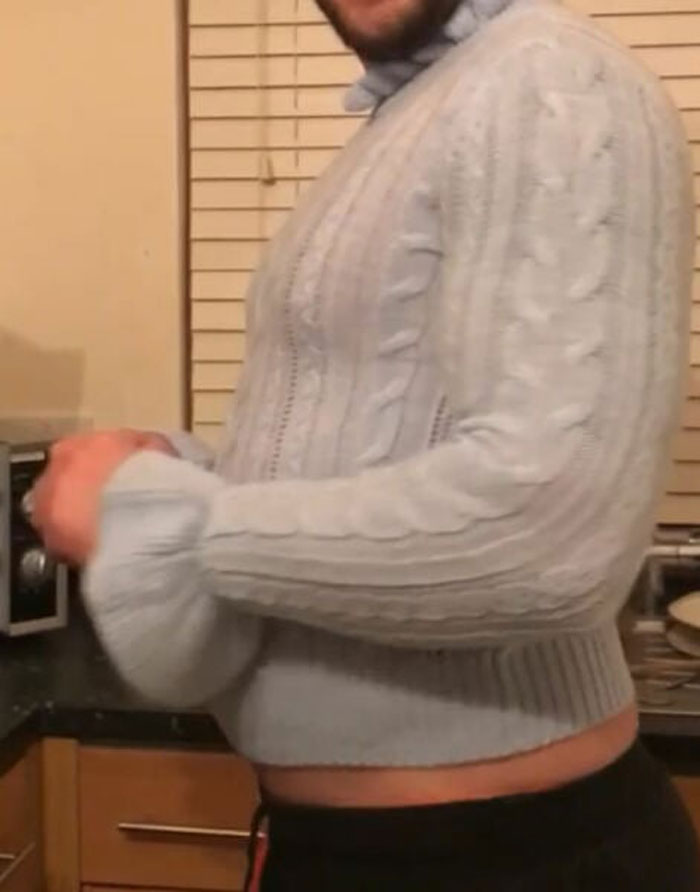 Person wearing a light blue knit sweater that looks like a mums bad birthday presents joke in a kitchen setting.