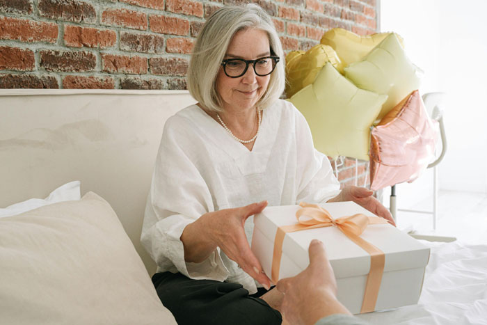 Older woman with glasses receiving a wrapped gift, illustrating mums bad birthday presents and family celebrations.