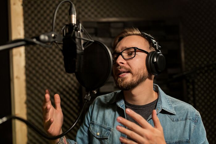 A man wearing glasses and headphones speaks into a microphone sharing stories of people who lost jobs to AI.
