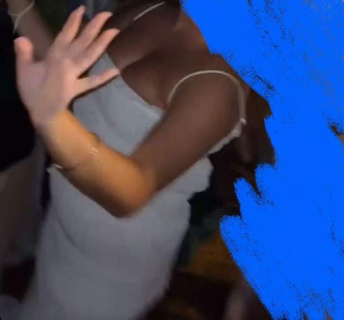 Woman in a long white dress raising her hand, captured at a wedding, highlighting bride horrified by cousin's attire.