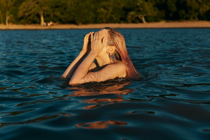 Person in water shielding face with hands, symbolizing moments the universe protected people from harm.