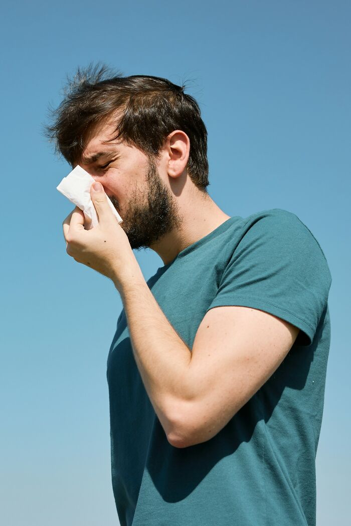A man with a beard in a teal shirt sneezing outdoors, illustrating karma striking with zero mercy concept.
