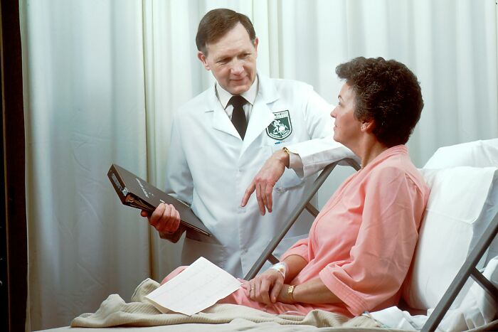 Doctor in white coat consulting female patient in hospital bed, discussing strange and dumb health hacks shared by patients.