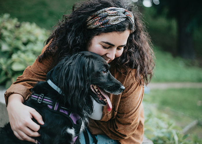 Young woman hugging her black dog outdoors, illustrating pet ownership rules conflict involving HOA board member.