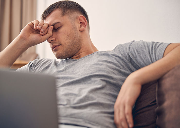 Stressed man sitting on a couch with laptop, frustrated over HOA board member refusing to follow pet ownership rules.