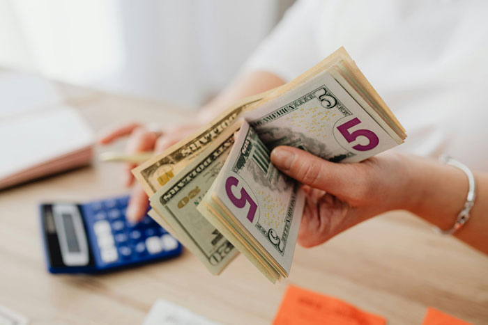 Person holding cash while another uses a calculator, representing fraud concerns during medical leave walks.