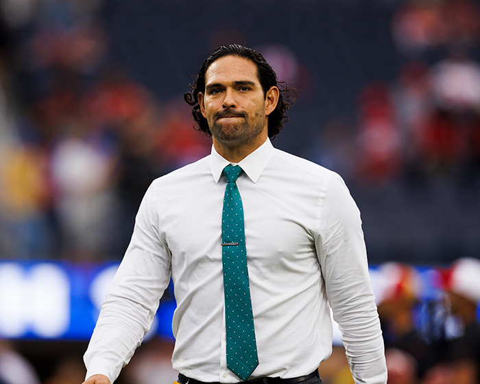 Mark Sanchez in a white shirt and teal tie walking on a field, linked to disturbing footage of bizarre behavior before attack.