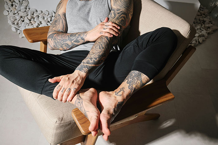 Man with extensive arm and leg tattoos sitting cross-legged in a chair, reflecting on relationship red flags.