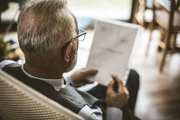 Older man wearing glasses reading a document indoors, symbolizing reflection on red flags in relationships.