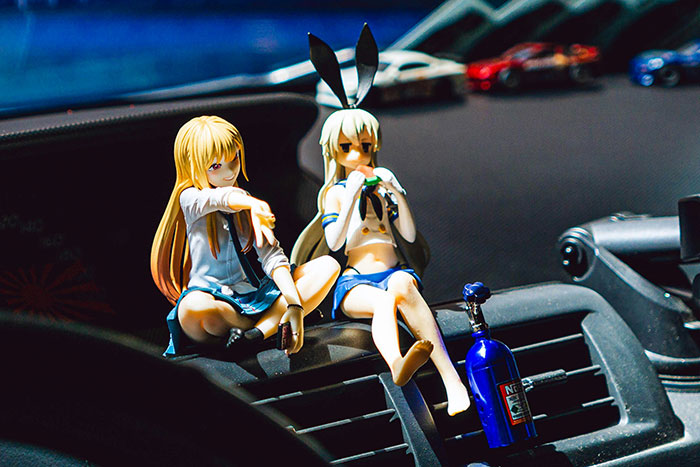 Two anime figures sitting on a car dashboard, illustrating women’s relationship red flags and emotional awareness.