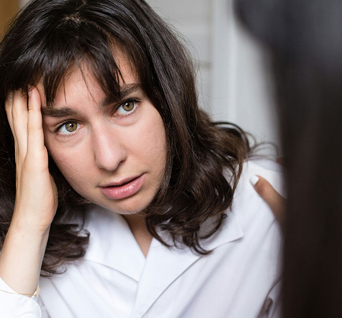 Stressed woman with dark hair holding head, upset during a serious conversation about group activities and neighbors.