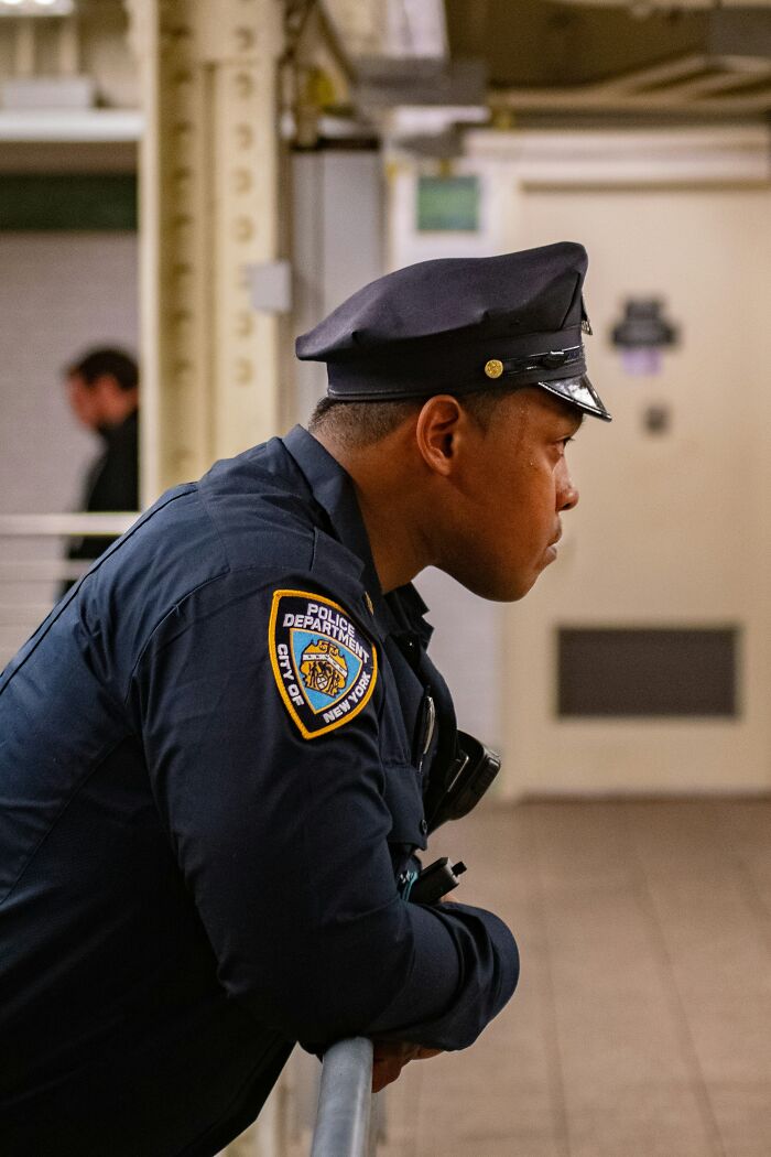 NYPD officer leaning on railing in subway station, illustrating people ask Americans about real life truths.