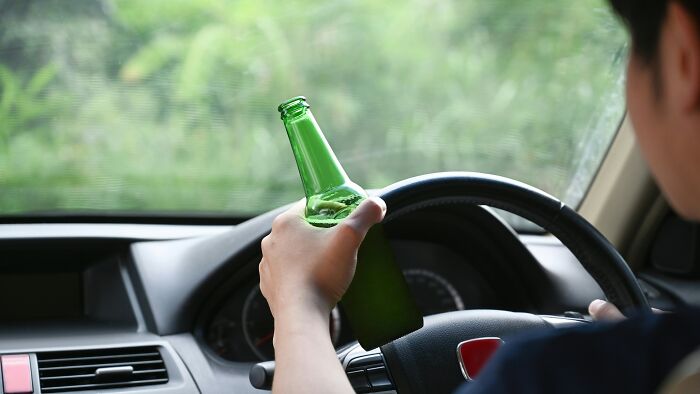 Man holding a green bottle while driving, illustrating people ask Americans if these things are true in real life concept.