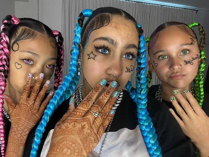 Three young women with colorful braided hair and face tattoos, highlighting Kanye West&rsquo;s warning about North&rsquo;s online life.