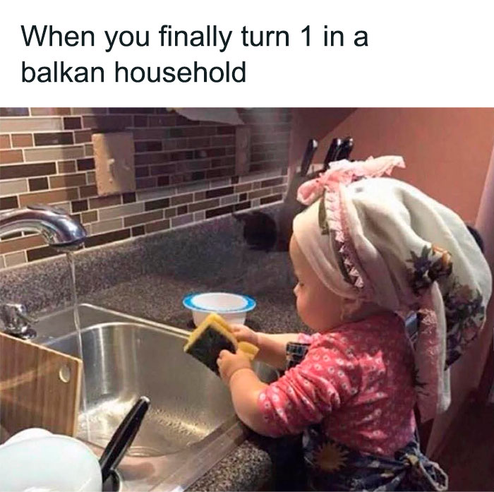 Toddler washing dishes at a kitchen sink depicting humor relatable to people raised in Eastern Europe and Balkan households.