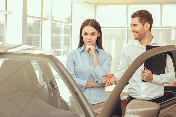Woman considering a new car purchase at a dealership, using car accident settlement money to buy a vehicle.