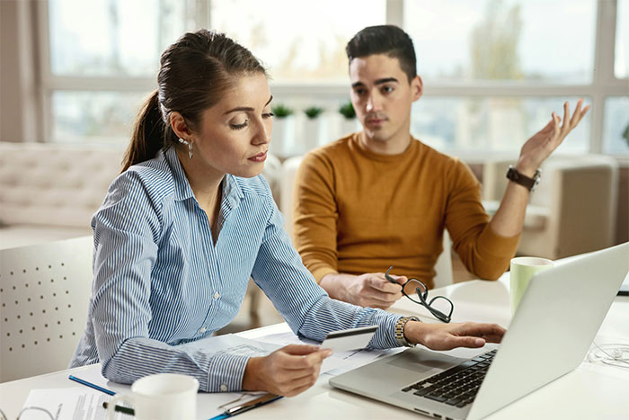 Woman using car accident settlement money on laptop while man gestures in disagreement in a bright office setting