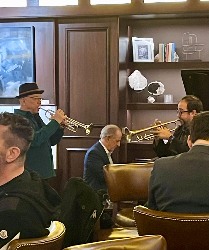 Two men playing trumpets while a third man plays piano in a room, an unphotoshopped pic that looks fake but is real.