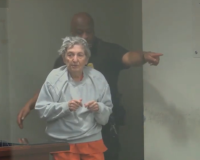 82-year-old woman in prison attire escorted by officer, linked to fatal attack on her husband and handwritten notes evidence