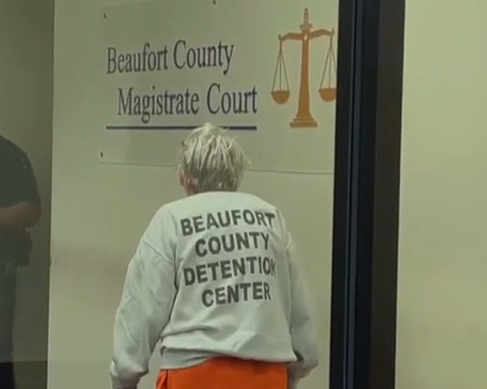 82-year-old woman in detention center clothing entering Beaufort County Magistrate Court after fatal attack on husband.