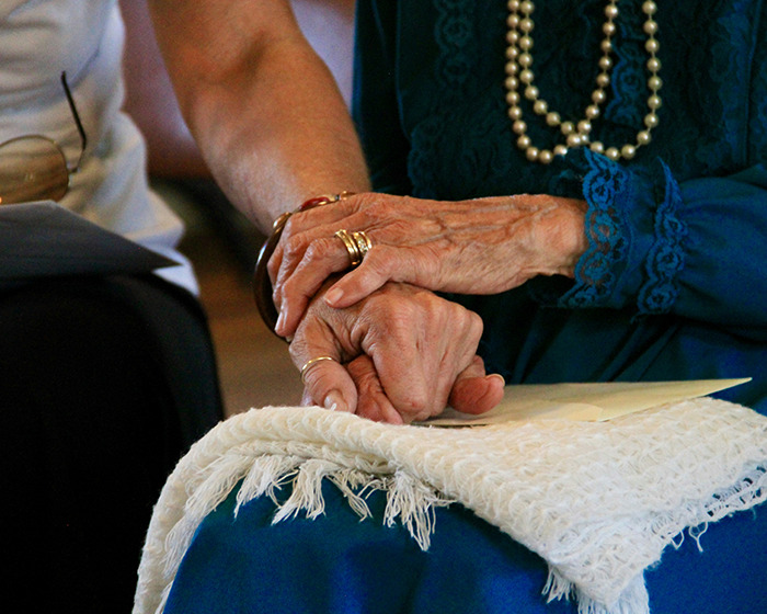 Elderly woman holding hands, wearing pearls and lace, symbolizing the 82-year-old woman fatally attacking her husband story.
