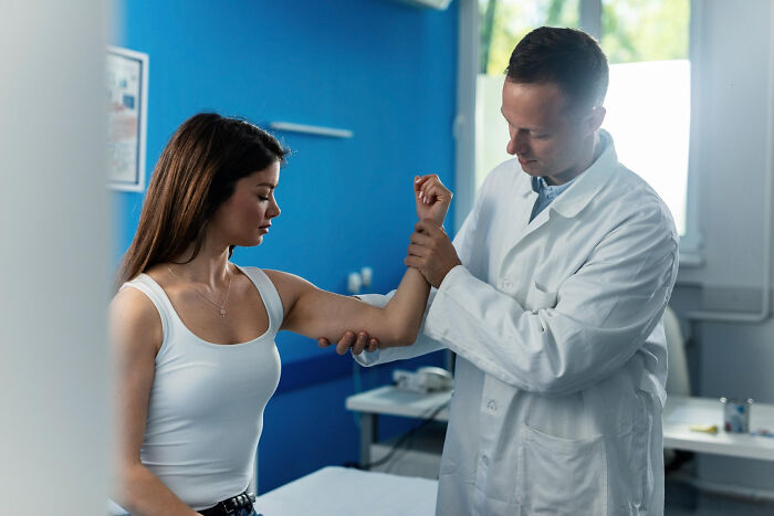 Doctor examining female patient’s arm in clinic, highlighting patients brushing off terrifying symptoms as normal.