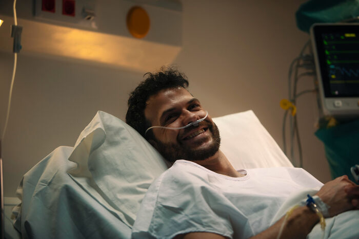 Man smiling in hospital bed with oxygen tube, highlighting patients brushing off terrifying symptoms as normal to doctors