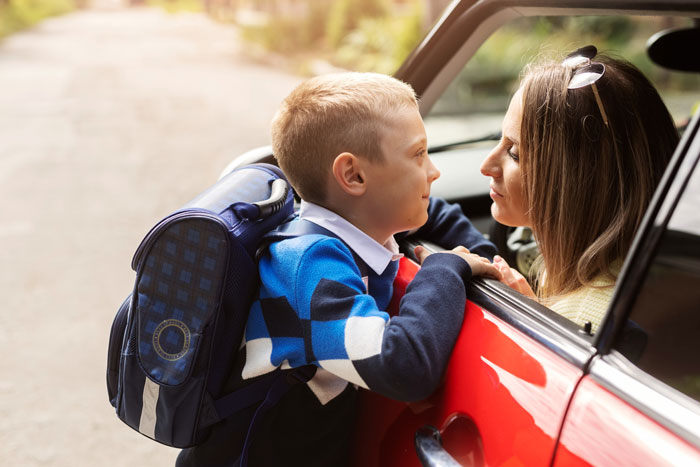 Child with backpack talking to woman in car near daycare, capturing the greedy daycare manager and parking lot chaos.