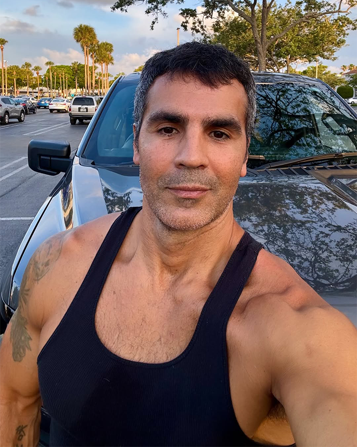 Man in a black tank top taking a selfie outdoors by a parked car, related to Jennifer Lopez's ex-husband cheating accusation.