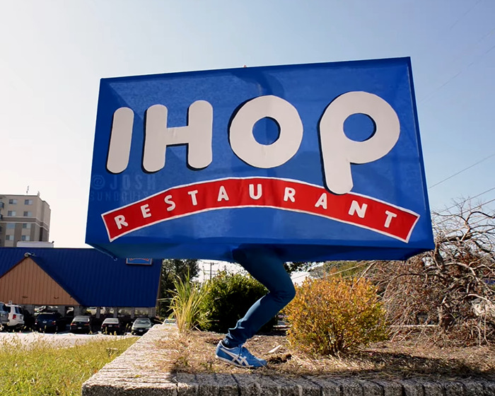 One-legged man in creative Halloween costume dressed as a giant IHOP restaurant sign outdoors.