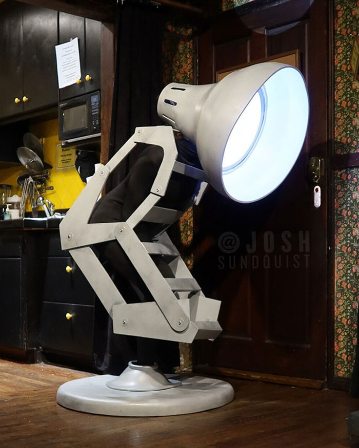 One-legged man in creative Halloween costume resembling a large adjustable desk lamp in a vintage kitchen setting