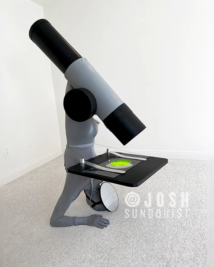 One-legged man wearing a creative Halloween costume designed as a giant microscope with detailed features indoors.