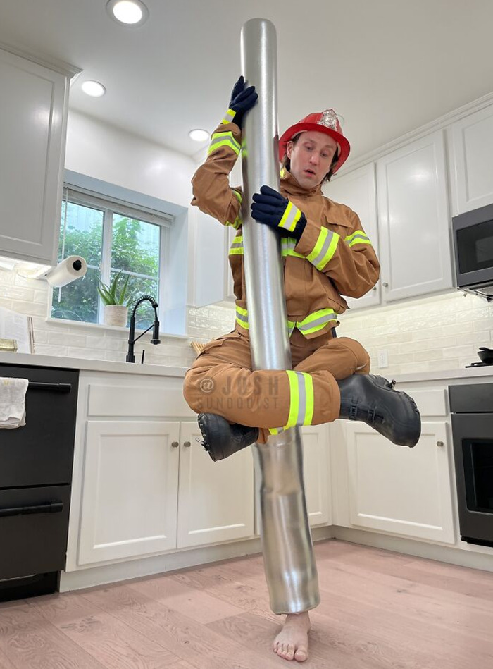 One-legged man in a creative firefighter Halloween costume holding a silver pole in a modern kitchen setting.