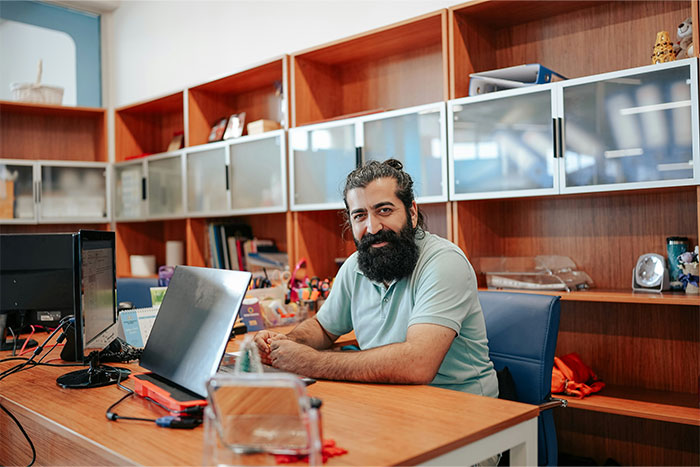 Man with long hair and beard sitting at a desk with laptop and monitors, illustrating clueless things young people say.