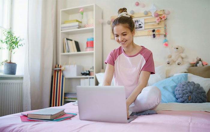 Teen girl smiling while using laptop on bed, illustrating clueless things young people have said online.