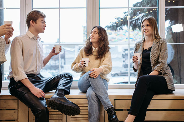 Three young people casually chatting and drinking coffee, reflecting clueless things young people have said.