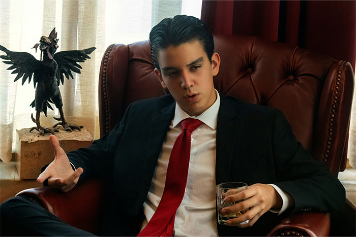 Young man in a suit and red tie sitting in a leather armchair, holding a glass, appearing deep in thought about clueless sayings.