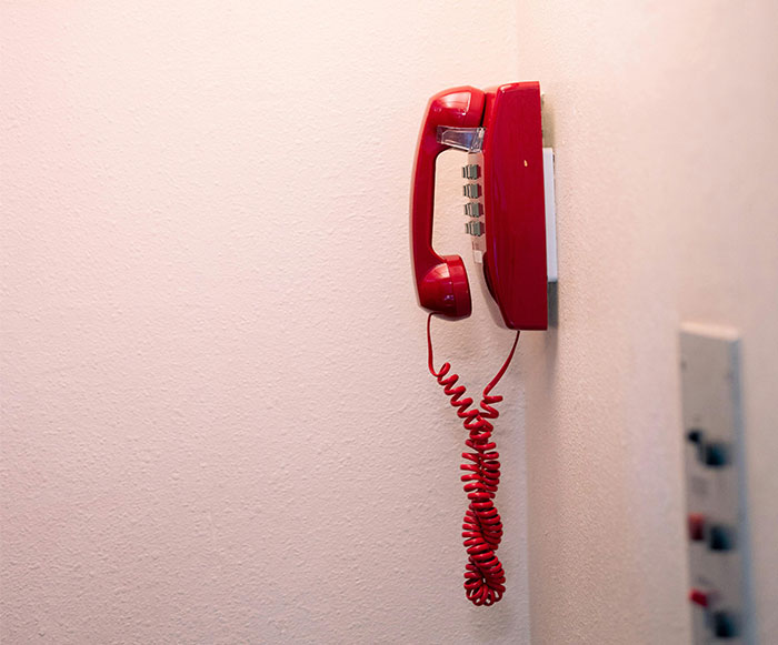 Red wall-mounted telephone with coiled cord against a beige wall, illustrating outdated technology and credit card misconceptions.