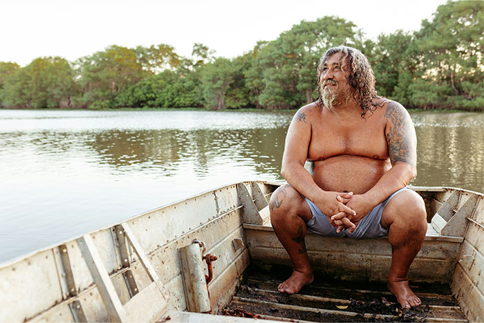 Middle-aged man sitting shirtless in a boat on the river, reflecting the idea of credit card and free money misconceptions.