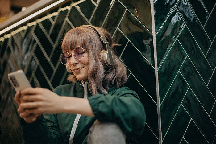 Young person wearing headphones and glasses, smiling while using a smartphone, capturing clueless things young people say.