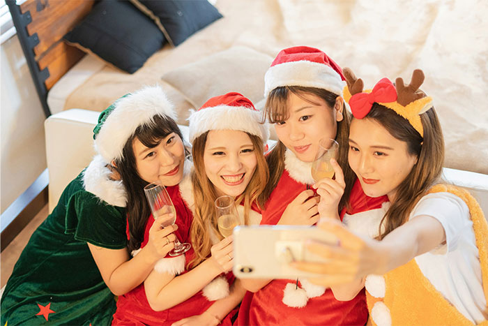 Four young women in festive holiday outfits taking a selfie while holding drinks, showing out of touch credit card mindset.