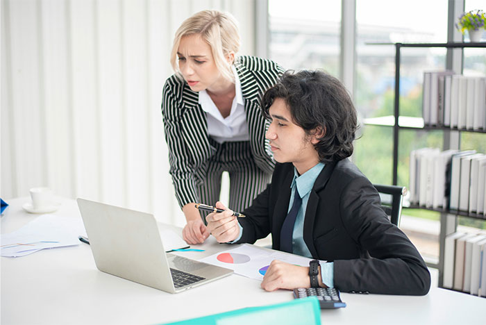Young professionals in business attire reviewing charts on a laptop, highlighting clueless things young people said.
