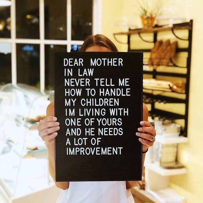 Person holding a sign about parenting challenges and mother-in-law advice, highlighting chaos and love in parenting.