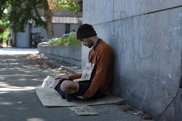 Young man sitting outside on a sidewalk, appearing homeless after parents kicked out teen, wearing a beanie and brown jacket. Young man sitting outside on a sidewalk, appearing homeless after parents kicked out teen, wearing a beanie and brown jacket.
