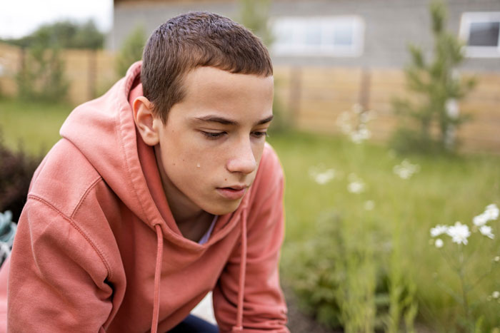 Teen in a pink hoodie with a tear on his cheek, sitting outside looking sad after parents kicked out teen from home. Teen in a pink hoodie with a tear on his cheek, sitting outside looking sad after parents kicked out teen from home.
