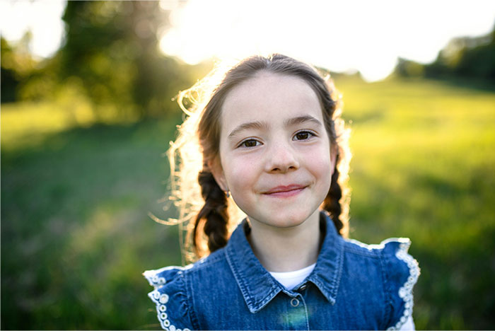 Smiling young girl with braided hair outdoors in sunlight, representing baby names parents regret giving their kids.