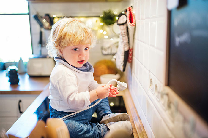Toddler sitting on kitchen counter with a curious expression, related to parents regretting baby names they chose.