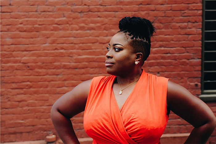 Woman in an orange dress standing confidently against a brick wall, reflecting on baby names parents regret giving.