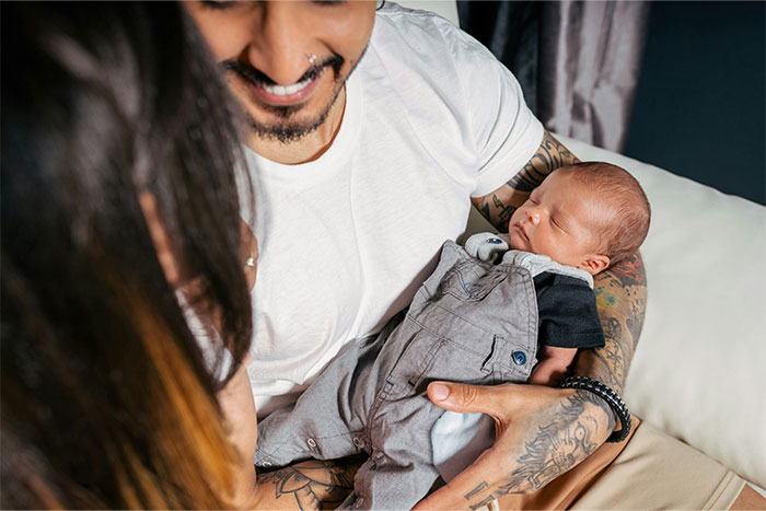 Father smiling and holding newborn baby while mother looks on, reflecting on baby names they regret giving their kids.