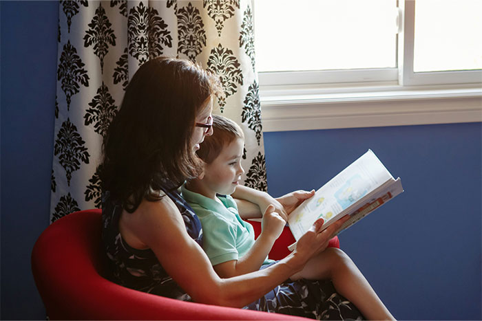 Mother and child sitting in a red chair reading a book together, illustrating parents reflecting on baby names they regret.